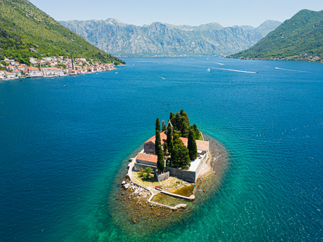 Aerial view of the island of Our Lady of the Rocks with its historic church and cypress trees surrounded by the blue waters of the Bay of Kotor in Perast Kotor Municipality Montenegro. Aerial view of the island of Our Lady of the Rocks with its historic church and cypress trees surrounded by the blue waters of the Bay of Kotor in Perast Kotor Municipality Montenegro.