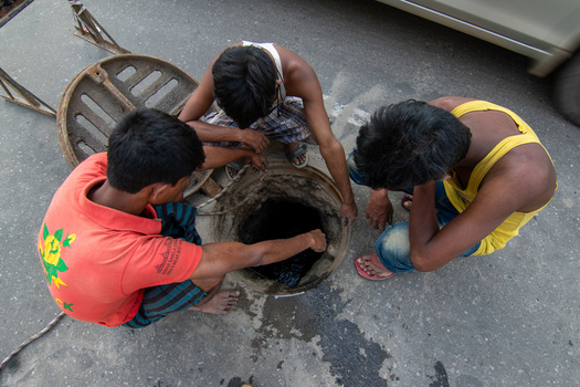 Dhaka Bangladesh 18 April 2018 View of three workers cleaning an open manhole on a city street with a car passing by. Dhaka Bangladesh 18 April 2018 View of three workers cleaning an open manhole on a city street with a car passing by.