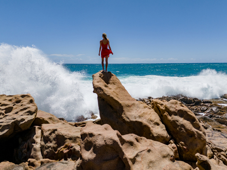 Aerial view of a woman in a red dress standing on a rock at Injidup Natural Spa with crashing waves in Yallingup Western Australia Australia. Aerial view of a woman in a red dress standing on a rock at Injidup Natural Spa with crashing waves in Yallingup Western Australia Australia.