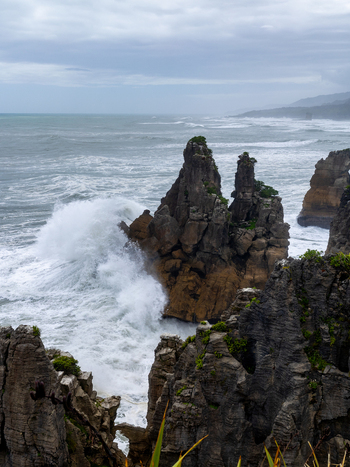 View of powerful waves crashing against the rugged dark rock formations under an overcast sky creating a dramatic coastal scene Pancake Rocks West Coast Region New Zealand. View of powerful waves crashing against the rugged dark rock formations under an overcast sky creating a dramatic coastal scene Pancake Rocks West Coast Region New Zealand.