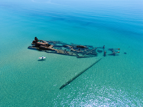 Aerial view of the Shipwreck Epanomi submerged in crystal clear turquoise water with a person on a paddleboard nearby in Epanomi Greece.