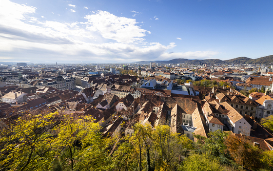 View of a vibrant cityscape unfolds with a tapestry of red tiled roofs nestled amidst verdant trees under a bright sky Graz Styria Austria. View of a vibrant cityscape unfolds with a tapestry of red tiled roofs nestled amidst verdant trees under a bright sky Graz Styria Austria.