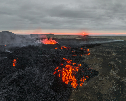 Aerial view of glowing lava flows from a volcanic eruption with smoke and steam rising against a sunset horizon in Iceland. Aerial view of glowing lava flows from a volcanic eruption with smoke and steam rising against a sunset horizon in Iceland.