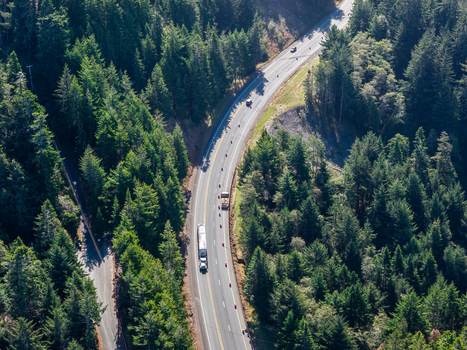Aerial view of road construction along a winding highway through a dense evergreen forest with traffic cones and a construction vehicle in Gold Beach Oregon United States. Aerial view of road construction along a winding highway through a dense evergreen forest with traffic cones and a construction vehicle in Gold Beach Oregon United States.