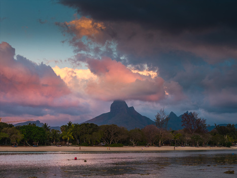 Aerial view of the Pieter Both mountain peak partially covered by pink and orange sunset clouds above a sandy beach with people and tropical trees in Moka District Mauritius. Aerial view of the Pieter Both mountain peak partially covered by pink and orange sunset clouds above a sandy beach with people and tropical trees in Moka District Mauritius.