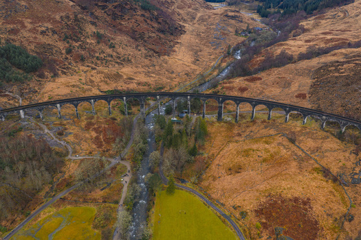 Aerial view of the Glenfinnan Viaduct with its iconic stone arches spanning across a rugged valley and river in the Scottish Highlands Glenfinnan Scotland United Kingdom.