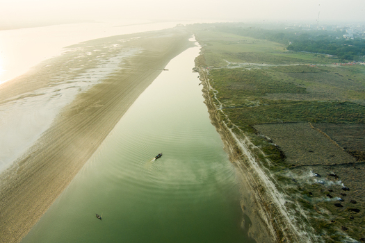 Aerial view of the Padma River with small boats navigating the calm waters near the sandy banks and green fields of Rajshahi Rajshahi Division Bangladesh.