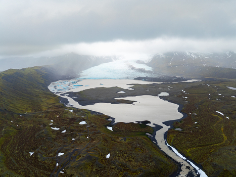 Aerial view of Kviarjokull glacier with its glacial lagoon dark volcanic sand and moss covered terrain under a cloudy sky in Kviarjokull Iceland.