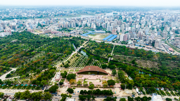 Aerial view of Rayer Bazaar Memorial with its curved brick structure and reflecting pool surrounded by parkland and the dense urban skyline of Dhaka Dhaka Division Bangladesh.