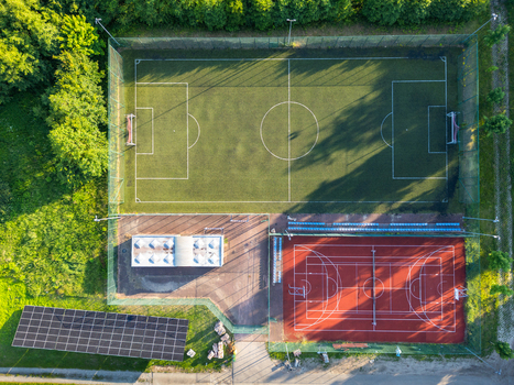 Aerial view of a sports complex featuring a green soccer field and a red multi purpose court with solar panels nearby in Suchacz Warmian Masurian Voiv Poland. Aerial view of a sports complex featuring a green soccer field and a red multi purpose court with solar panels nearby in Suchacz Warmian Masurian Voiv Poland.