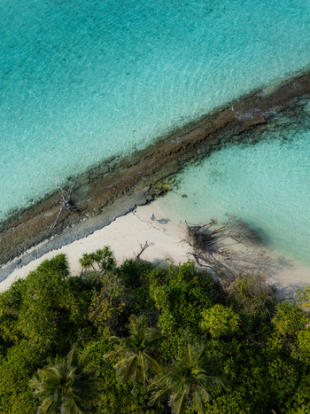 Aerial view of a vibrant contrast between the lush greenery and the turquoise waters of the island s shore Thuraakunu Thiladhunmathee Uthuruburi Maldives. Aerial view of a vibrant contrast between the lush greenery and the turquoise waters of the island s shore Thuraakunu Thiladhunmathee Uthuruburi Maldives.