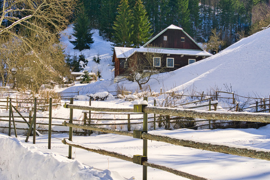 View of a rustic wooden house nestled amidst snow covered hills a serene winter landscape punctuated by bare trees and a weathered wooden fence Moce Banska Bystrica Region Slovakia.