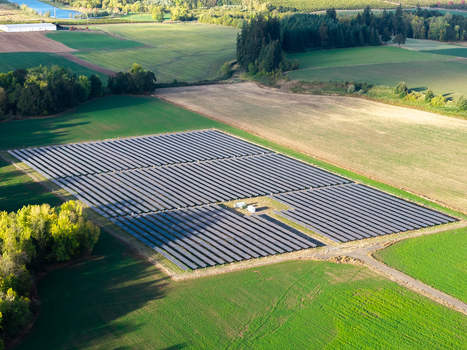 Aerial view of a large solar farm with rows of photovoltaic panels situated in a rural landscape surrounded by green fields and trees in Woodburn Oregon United States. Aerial view of a large solar farm with rows of photovoltaic panels situated in a rural landscape surrounded by green fields and trees in Woodburn Oregon United States.