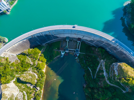 Aerial view of the Barrage de Rossens dam wall curving over the turquoise waters of Lac de la Gruyere surrounded by lush green forests in Pont la Ville Fribourg Switzerland.
