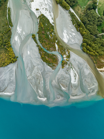 Aerial view of braided river patterns where glacial waters meet the turquoise lake creating a stunning contrast against the green shoreline Glenorchy Otago Region New Zealand. Aerial view of braided river patterns where glacial waters meet the turquoise lake creating a stunning contrast against the green shoreline Glenorchy Otago Region New Zealand.