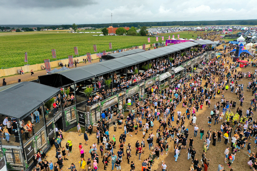 Herzogenaurach Germany 26 July 2025 Aerial view of Open Beatz Festival with large crowds of people gathered near temporary structures and green fields under a cloudy sky.
