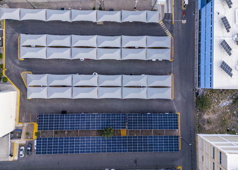 Aerial view of solar panel carports and rooftop solar arrays installed in a parking lot with white shade structures and industrial buildings in Chihuahua Chihuahua Mexico. Aerial view of solar panel carports and rooftop solar arrays installed in a parking lot with white shade structures and industrial buildings in Chihuahua Chihuahua Mexico.