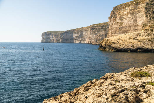 View of the towering limestone cliffs and deep blue Mediterranean waters at Xlendi Bay Zebbug Gozo Region Malta.