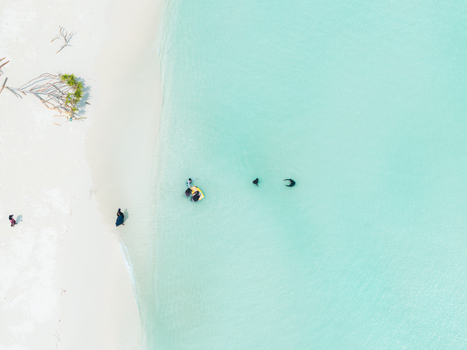 Aerial view of a dazzling white sand beach kissing vibrant turquoise waters dotted with people Thuraakunu Thiladhunmathee Uthuruburi Maldives. Aerial view of a dazzling white sand beach kissing vibrant turquoise waters dotted with people Thuraakunu Thiladhunmathee Uthuruburi Maldives.
