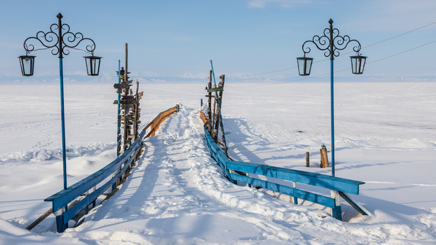 View of Goryachiye Istochniki Khakusy featuring a snow covered pier with blue railings extending into frozen Lake Baikal in Severobaykal skiy Rayon Respublika Buryatiya Russia. View of Goryachiye Istochniki Khakusy featuring a snow covered pier with blue railings extending into frozen Lake Baikal in Severobaykal skiy Rayon Respublika Buryatiya Russia.
