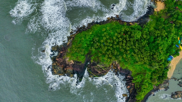 Aerial view of the rocky coastline at Palolem Beach with lush palm trees crashing waves and sandy shores in Canacona Goa India.