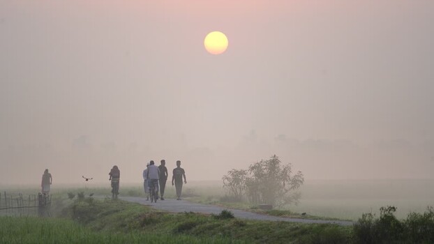 View of people walking along a rural road at sunrise Bangladesh.