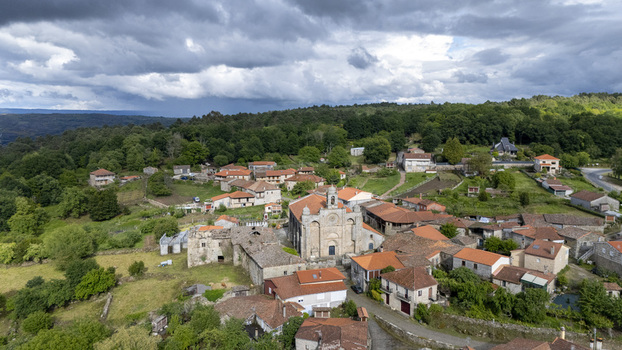 Aerial view of the historic Iglesia de Santa Marina de Augas Santas and traditional stone houses with red tiled roofs surrounded by lush green forests Augas Santas Ourense Spain. Aerial view of the historic Iglesia de Santa Marina de Augas Santas and traditional stone houses with red tiled roofs surrounded by lush green forests Augas Santas Ourense Spain.