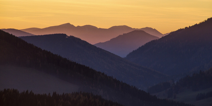 View of layers of blue tinged mountains fading into the horizon under a soft golden sky Sommeralm Steiermark Austria. View of layers of blue tinged mountains fading into the horizon under a soft golden sky Sommeralm Steiermark Austria.