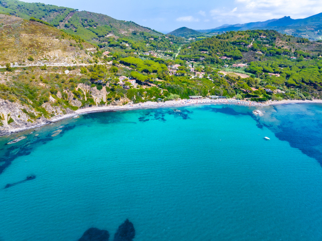 Aerial view of the turquoise bay sandy beach and lush green hills of the Mediterranean coastline in Capoliveri Tuscany Italy.