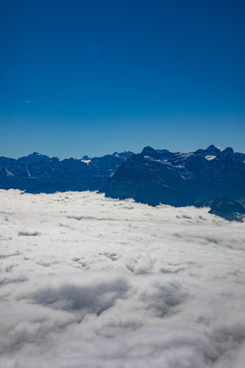 Aerial view of the Swiss Alps with jagged mountain peaks rising above a dense sea of clouds under a clear blue sky in Airolo Ticino Switzerland. Aerial view of the Swiss Alps with jagged mountain peaks rising above a dense sea of clouds under a clear blue sky in Airolo Ticino Switzerland.