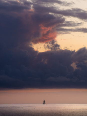 Aerial view of a lone sailboat on the calm ocean under a dramatic sunset sky with dark clouds off Moka District Mauritius. Aerial view of a lone sailboat on the calm ocean under a dramatic sunset sky with dark clouds off Moka District Mauritius.