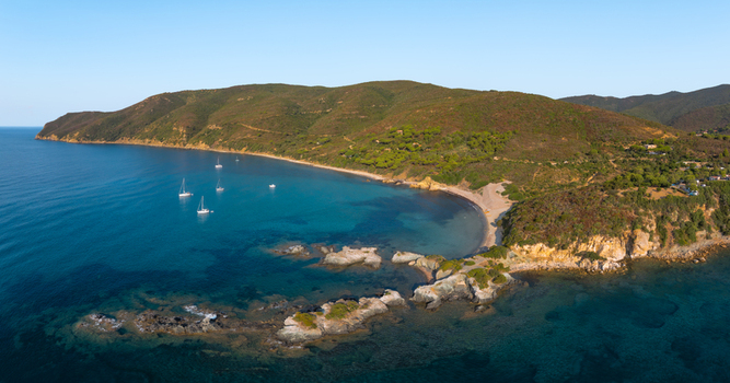 Aerial view of Lacona Beach with turquoise water rocky outcrops sailboats and green hills under a clear sky in Lacona Tuscany Italy.