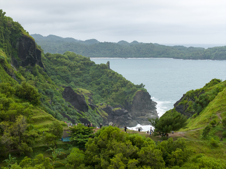Aerial view of lush green cliffs cascading down to meet the turquoise sea as people gather on the shore below at Pengilon Hill Gunungkidul Regency Daerah Istimewa Yogyakarta Indonesia. Aerial view of lush green cliffs cascading down to meet the turquoise sea as people gather on the shore below at Pengilon Hill Gunungkidul Regency Daerah Istimewa Yogyakarta Indonesia.