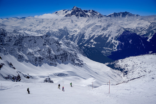 Aerial view of skiers descending a snowy slope at La Rosiere ski resort with majestic alpine peaks under a clear blue sky in Montvalezan Auvergne Rhone Alpes France.