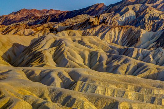 View of the rugged eroded badlands and golden hued hills of Death Valley National Park s backcountry under soft morning light in Death Valley California United States.