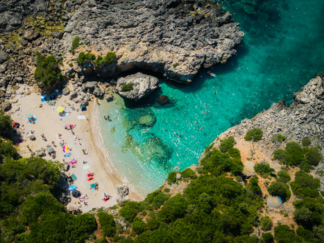Aerial view of Aquarium Beach with turquoise water rocky cliffs and people sunbathing on the sand in Jala Vlore County Albania. Aerial view of Aquarium Beach with turquoise water rocky cliffs and people sunbathing on the sand in Jala Vlore County Albania.