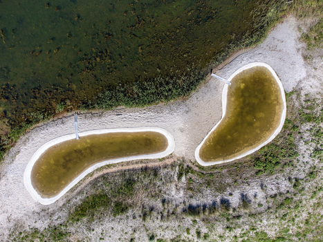 Aerial view of kidney shaped ponds with concrete borders reflecting sunlight in their shallow waters surrounded by sandy banks and green vegetation Almere Flevoland Netherlands.