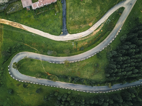 Aerial view of a dark winding road sharply contrasting with vibrant green hills and dense forest leading to buildings Obudu Cross River Nigeria.