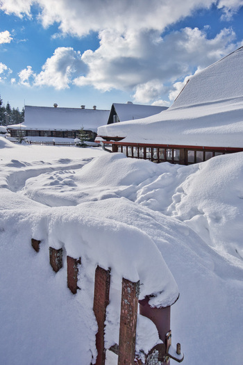 View of snow laden rooftops and fences create a winter wonderland with a bright blue sky and fluffy white clouds in the background Donovaly Slovakia. View of snow laden rooftops and fences create a winter wonderland with a bright blue sky and fluffy white clouds in the background Donovaly Slovakia.