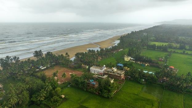 Aerial view of Gokarna beach with its sandy coastline lush green fields and surrounding buildings under a cloudy sky in Gokarna Karnataka India.