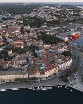 Aerial view of the historic Pula waterfront featuring the harbor with boats dense urban architecture with terracotta rooftops and coastal roads in Pula Istarska zupanija Croatia. Aerial view of the historic Pula waterfront featuring the harbor with boats dense urban architecture with terracotta rooftops and coastal roads in Pula Istarska zupanija Croatia.