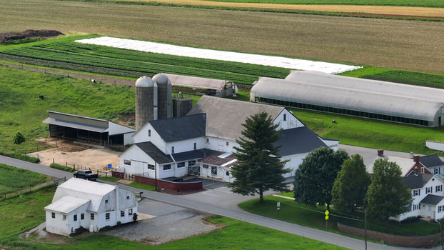 Aerial view of a traditional farmstead with a large white barn silos and greenhouses surrounded by lush agricultural fields in Leola Pennsylvania United States. Aerial view of a traditional farmstead with a large white barn silos and greenhouses surrounded by lush agricultural fields in Leola Pennsylvania United States.