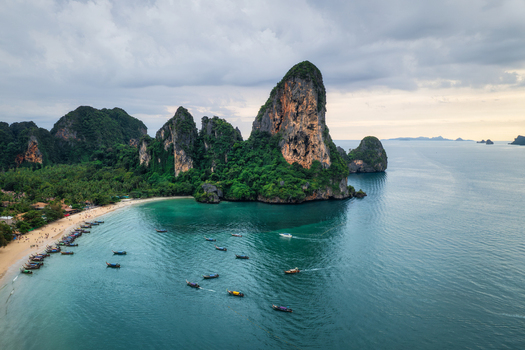 Aerial view of Railay Beach with limestone cliffs turquoise water and traditional long tail boats moored along the sandy shore in Ao Nang Krabi Thailand. Aerial view of Railay Beach with limestone cliffs turquoise water and traditional long tail boats moored along the sandy shore in Ao Nang Krabi Thailand.