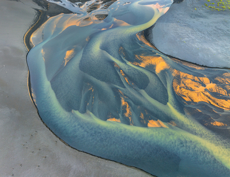 Aerial view of a glacial river delta with intricate sediment patterns and golden sunlight reflecting on sandbanks in Iceland. Aerial view of a glacial river delta with intricate sediment patterns and golden sunlight reflecting on sandbanks in Iceland.