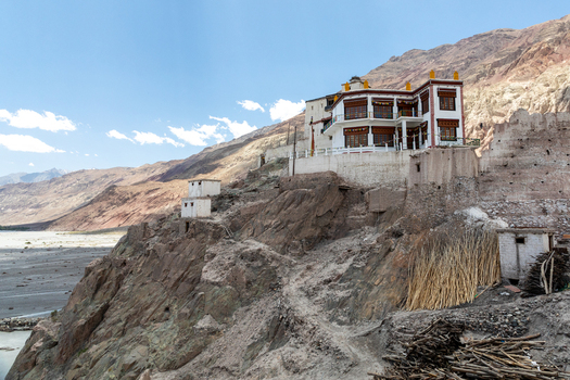 View of Charasa Gonpa perched on a rocky cliff overlooking a river valley with traditional architecture clear blue sky and rugged mountain terrain Charasa Ladakh India.