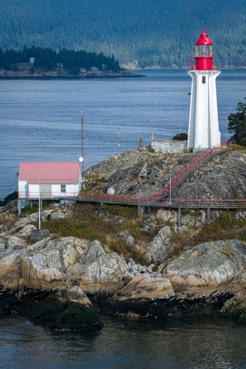 Aerial view of Point Atkinson Lighthouse with its red lantern room situated on a rocky coastline with a white keeper s house and metal walkways in West Vancouver British Columbia Canada.
