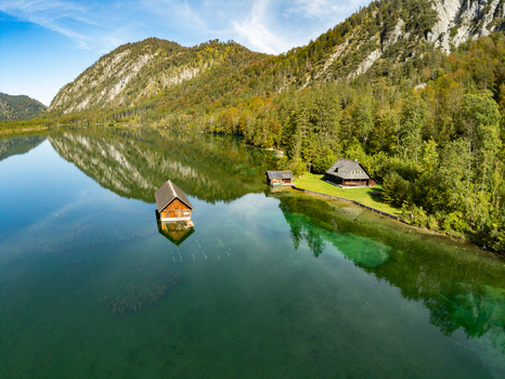 Aerial view of Attensee with a wooden boathouse floating on the clear turquoise water surrounded by lush green forests and steep mountains in Rottenbach Bayern Germany. Aerial view of Attensee with a wooden boathouse floating on the clear turquoise water surrounded by lush green forests and steep mountains in Rottenbach Bayern Germany.