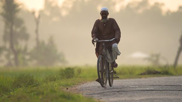 View of an elderly man riding a bicycle on a misty road Bangladesh.