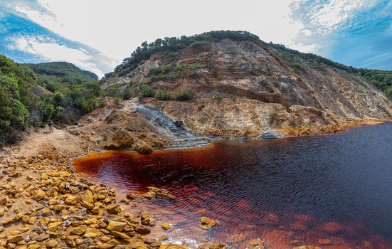 Aerial view of the Laghetto delle conche a striking red colored lake in a former mining area with rocky terrain and sparse vegetation in Rio Marina Toscana Italy.