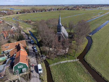 Aerial view of Hervormde Kerk s spire piercing the sky embraced by the bare trees a stark contrast to the lush green fields Krommenie Noord Holland Netherlands. Aerial view of Hervormde Kerk s spire piercing the sky embraced by the bare trees a stark contrast to the lush green fields Krommenie Noord Holland Netherlands.